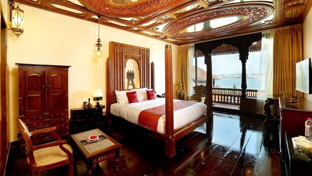 A spacious bedroom with a four-poster bed, wooden furniture, and a balcony with a view of the sea. - Ginger House Museum Hotel (Kochi)