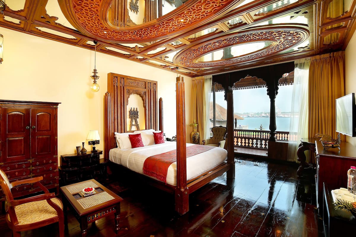 A spacious bedroom with a four-poster bed, wooden furniture, and a balcony with a view of the sea.