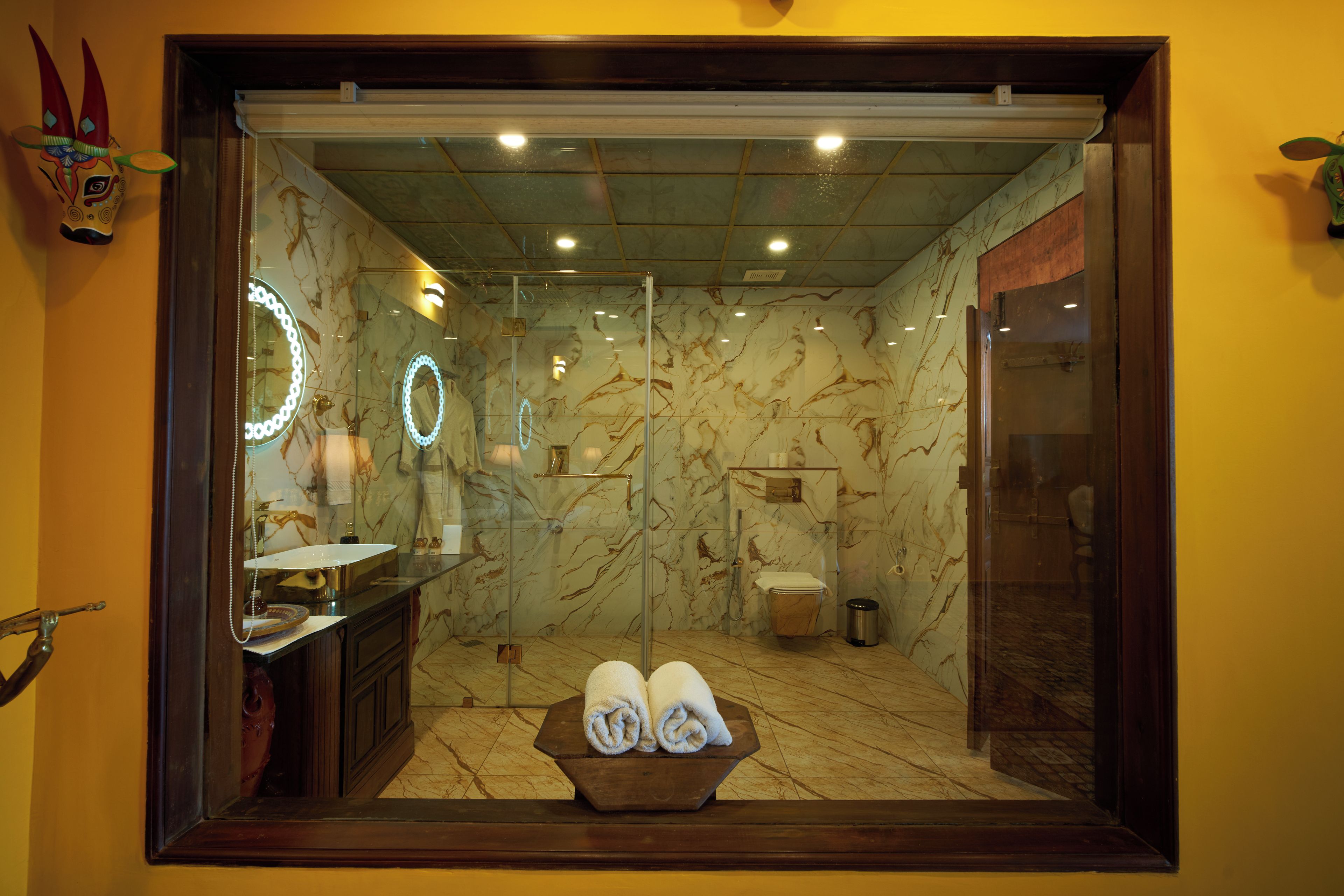 A bathroom with a marble floor, a glass-enclosed shower, a sink with a mirror, and a towel rack with towels.