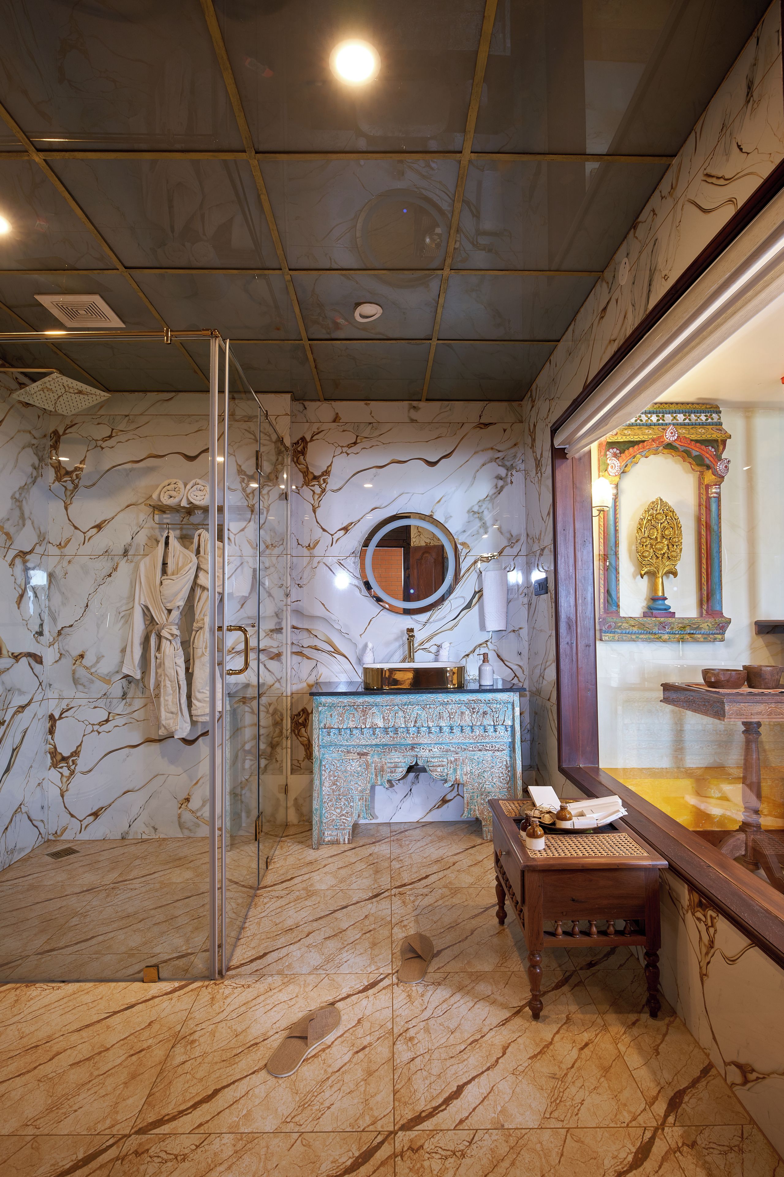 A bathroom with a glass shower enclosure, a marble-tiled wall, a vanity with a mirror, and a decorative archway.