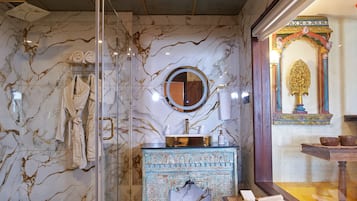 A bathroom with a glass shower enclosure, a marble-tiled wall, a vanity with a mirror, and a decorative archway.