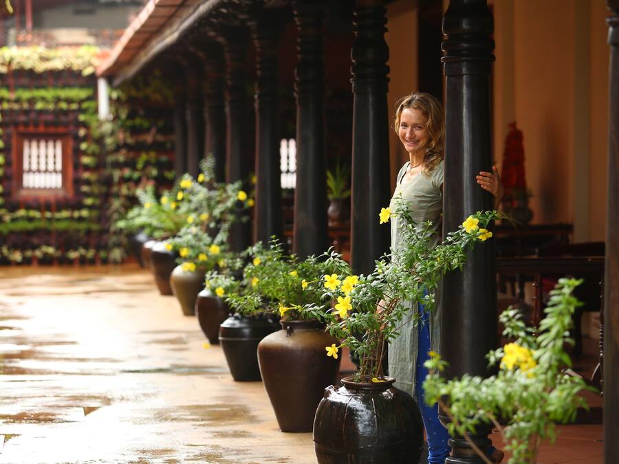 Un pasillo con una serie de grandes jarrones con flores amarillas, suelo de madera y un estilo arquitectónico tradicional con columnas.