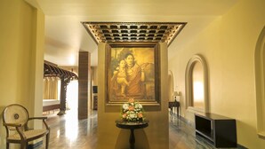 A hallway with a framed painting, a table with flowers, a chair, and a bench. - Ginger House Museum Hotel (Kochi)