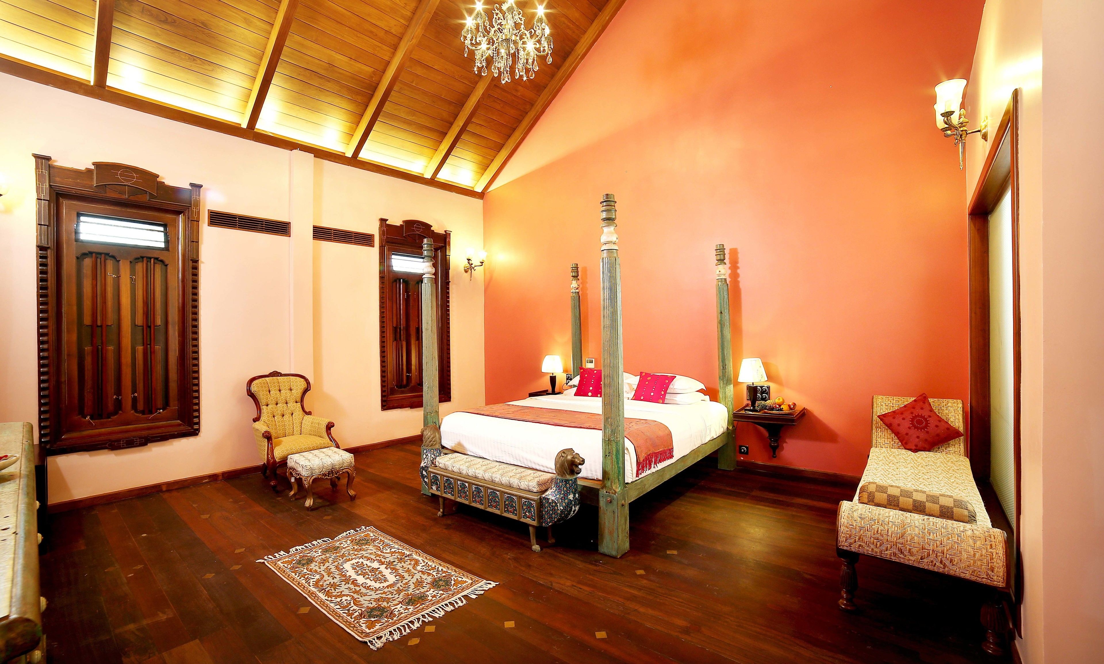 A four-poster bed with a dog statue, a wooden chair, a small table, and a chandelier in a room with wooden floors and a sloped ceiling.