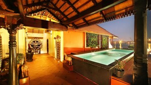 A pool area with a tiled floor, a large pool, and a covered section with a wooden roof. - Ginger House Museum Hotel (Kochi)