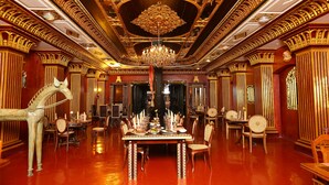 A luxurious dining room with ornate golden ceiling and walls, a large chandelier, and a long dining table set for a meal. - Ginger House Museum Hotel (Kochi)