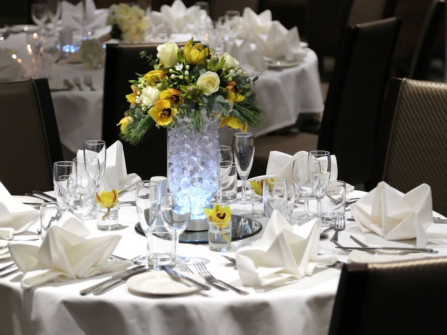 A dining table set for a formal meal with white tablecloths, folded napkins, and a floral centerpiece.