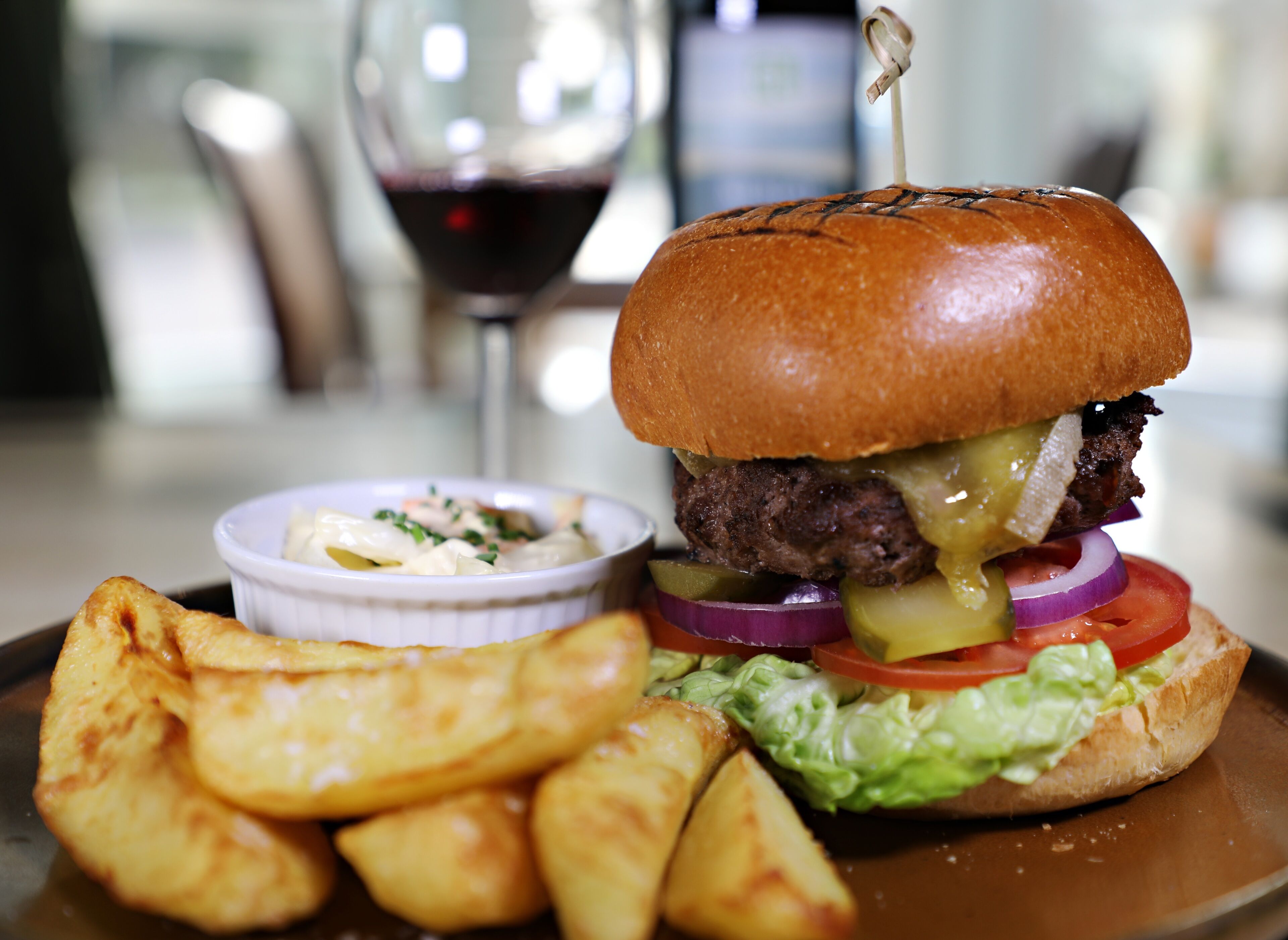 A burger with lettuce, tomato, and pickles, served with potato wedges and a side of coleslaw.