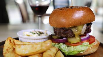 A burger with lettuce, tomato, and pickles, served with potato wedges and a side of coleslaw.