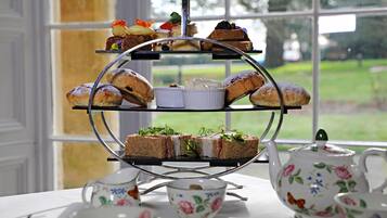 A three-tiered dessert stand with various pastries and sandwiches, set on a table with floral teacups and a teapot.