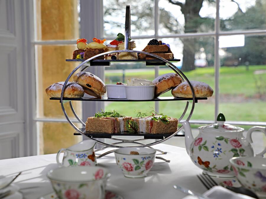 A three-tiered dessert stand with various pastries and sandwiches, set on a table with floral teacups and a teapot.