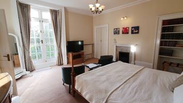 A hotel room with a large bed, a television, a fireplace, a bookshelf, and a view of the outdoors.