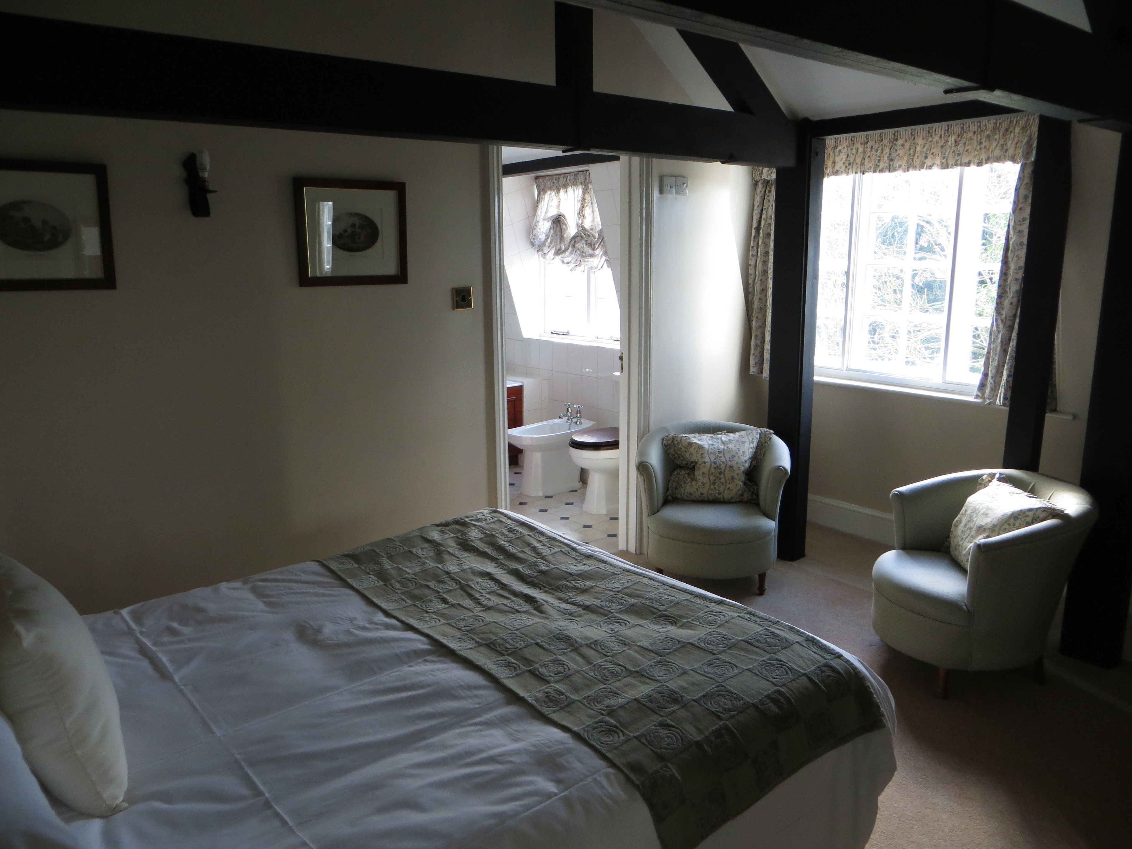 A bedroom with a bed, two chairs, a window, and a bathroom visible through an open door.