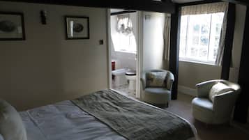 A bedroom with a bed, two chairs, a window, and a bathroom visible through an open door.