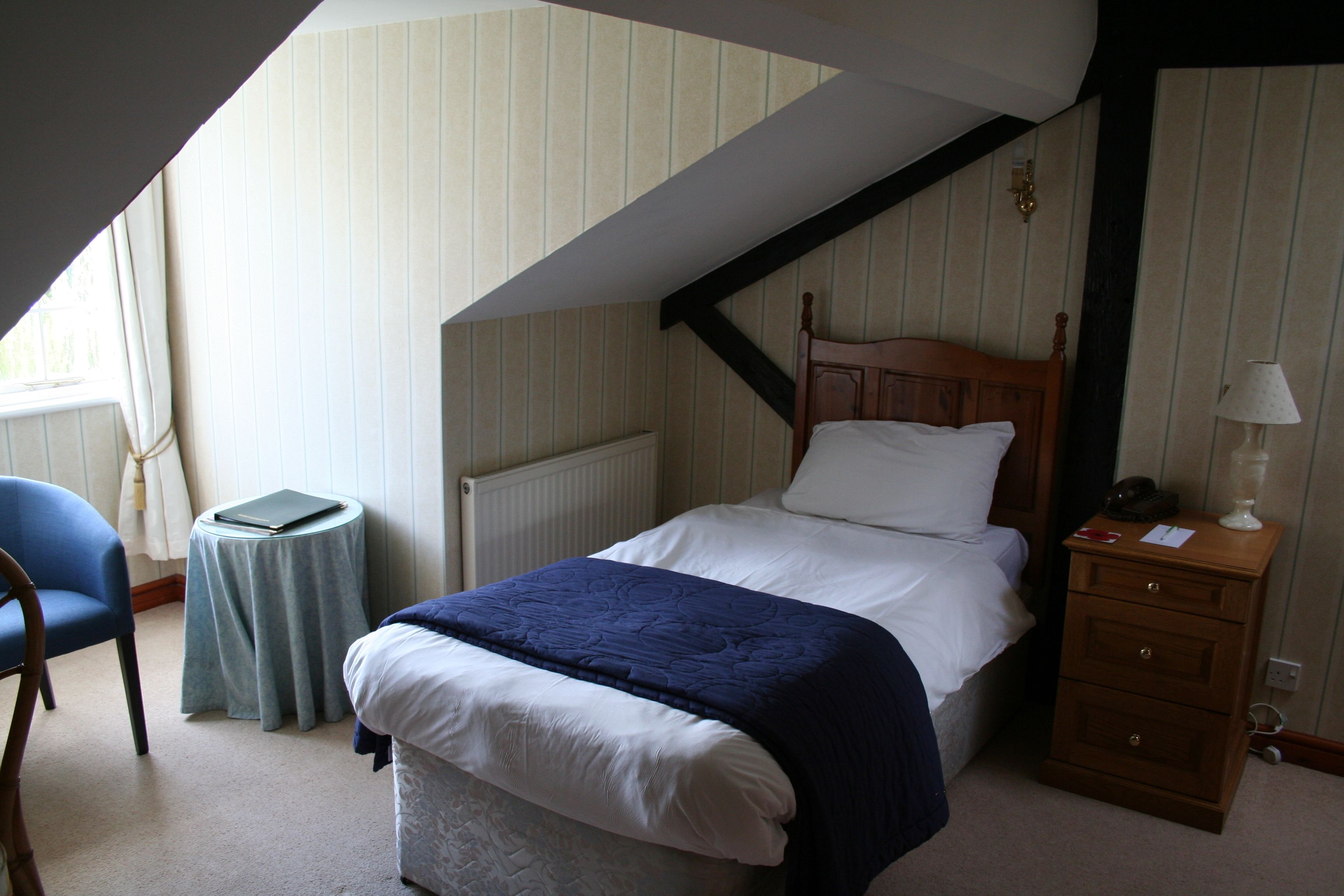 A bedroom with a bed, a nightstand, a chair, a small table, and a radiator.