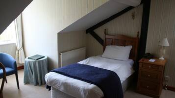 A bedroom with a bed, a nightstand, a chair, a small table, and a radiator.