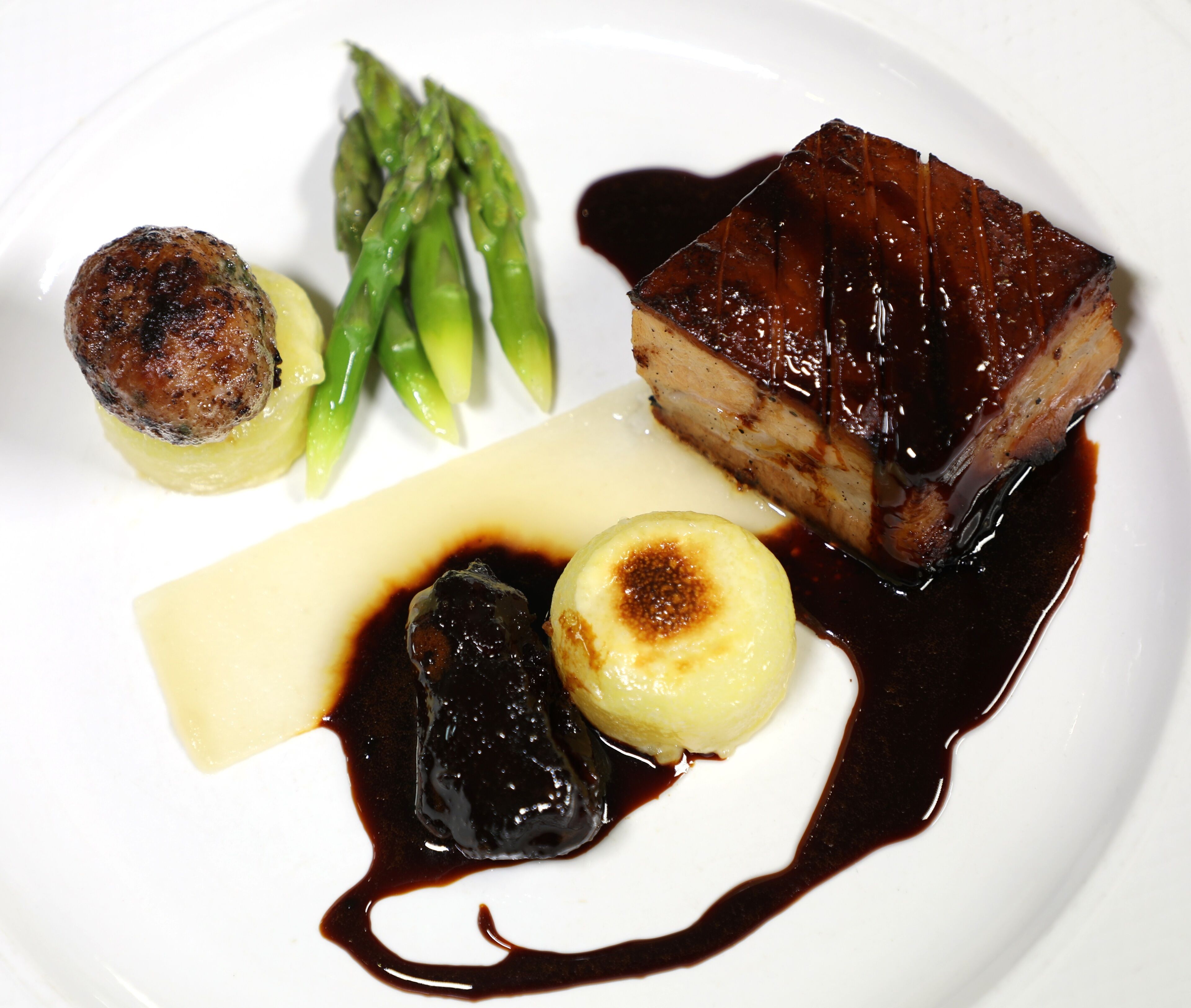 A plate with a piece of glazed meat, asparagus, a grilled vegetable, and a dessert item.