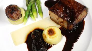 A plate with a piece of glazed meat, asparagus, a grilled vegetable, and a dessert item.