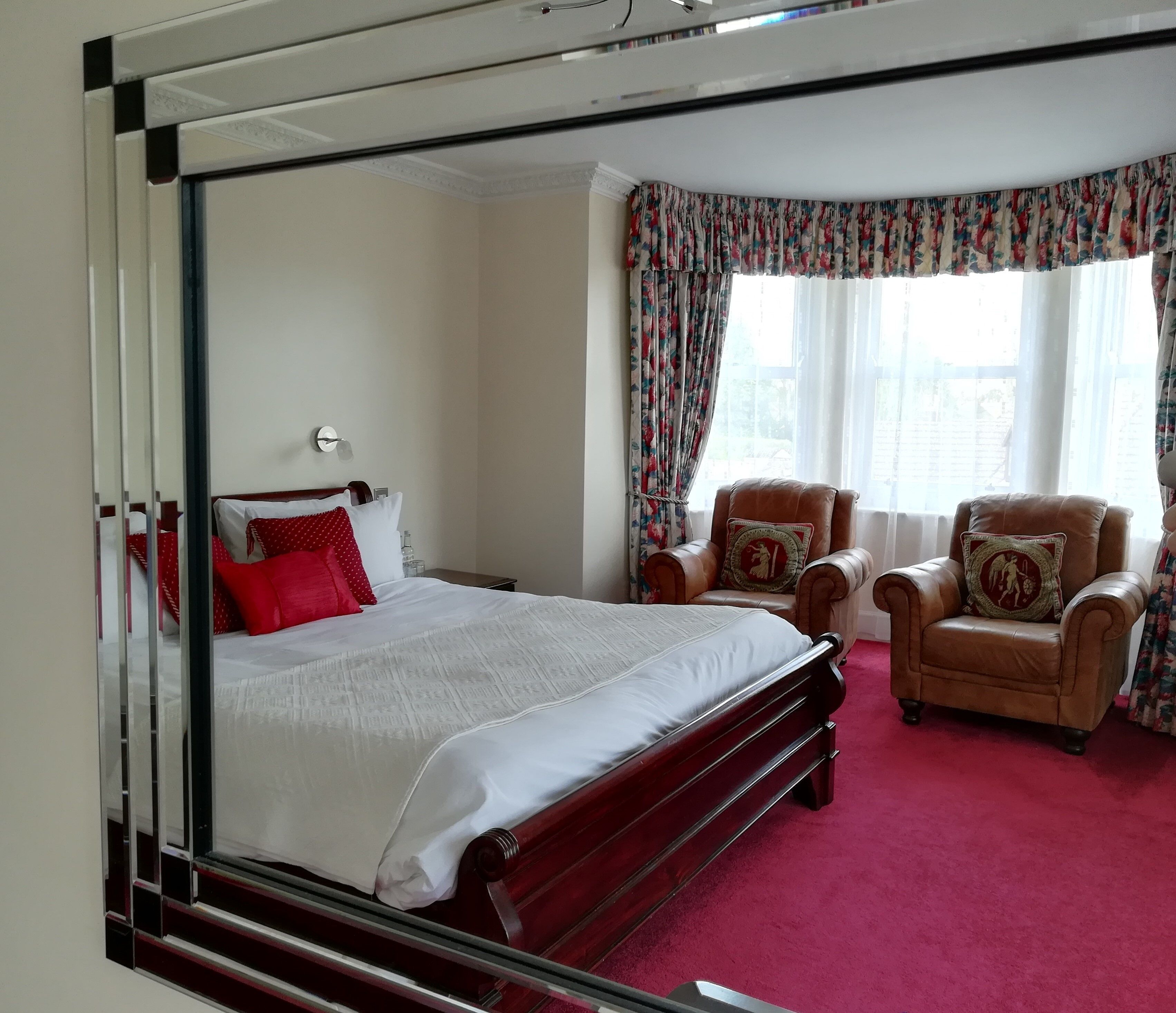A hotel room with a large bed, two leather armchairs, and a window with floral curtains.