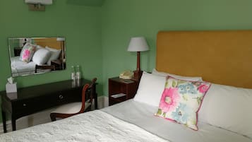 Una habitación de hotel con cama, escritorio, silla, mesita de noche, lámpara y espejo.