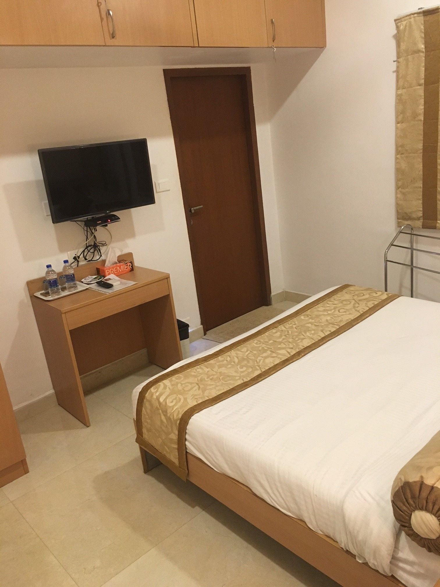 A hotel room with a bed, a desk with a television, a door, and a window with curtains.