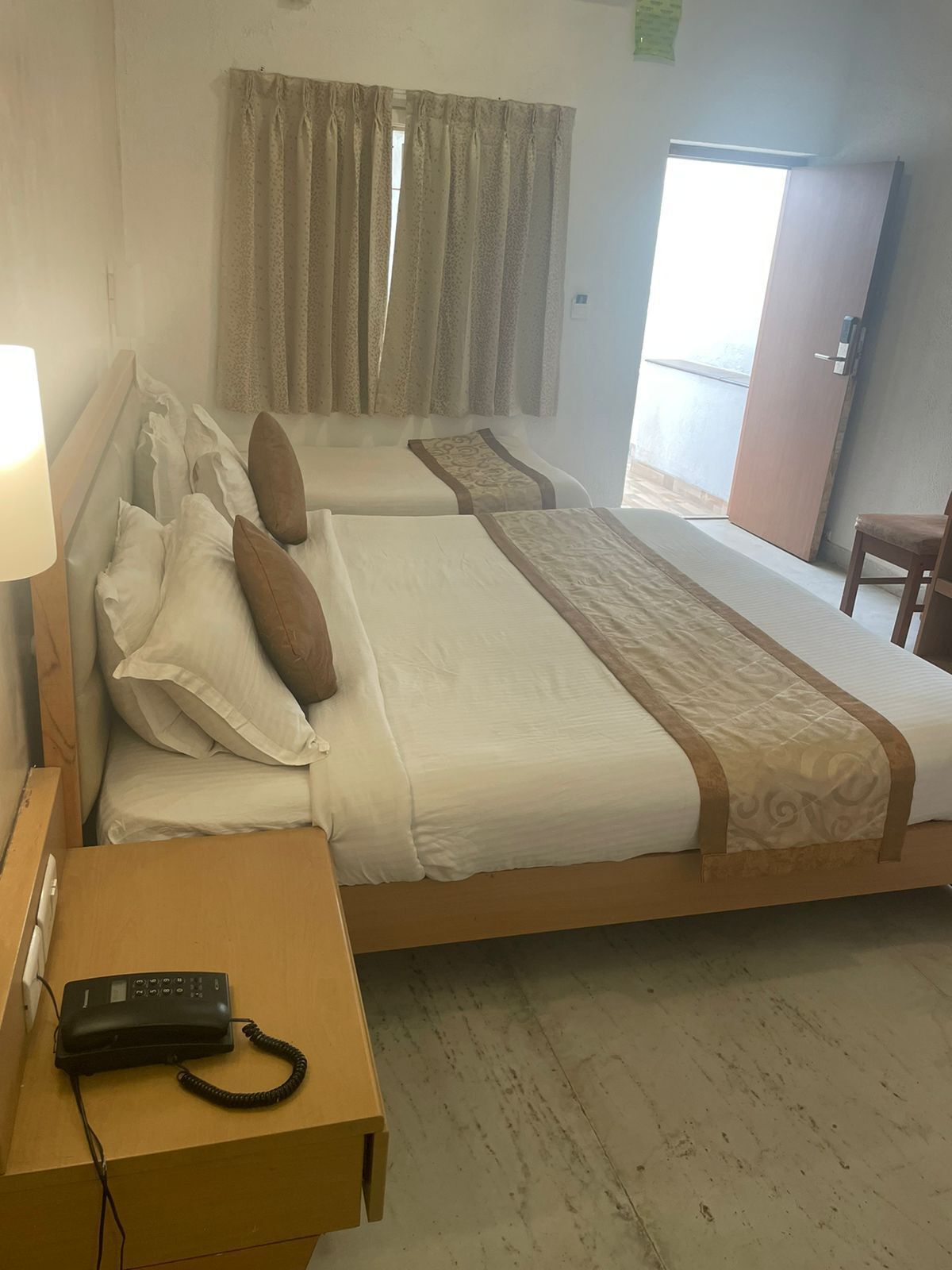 A hotel room with two beds, a bedside table with a phone, and a view of the outside.