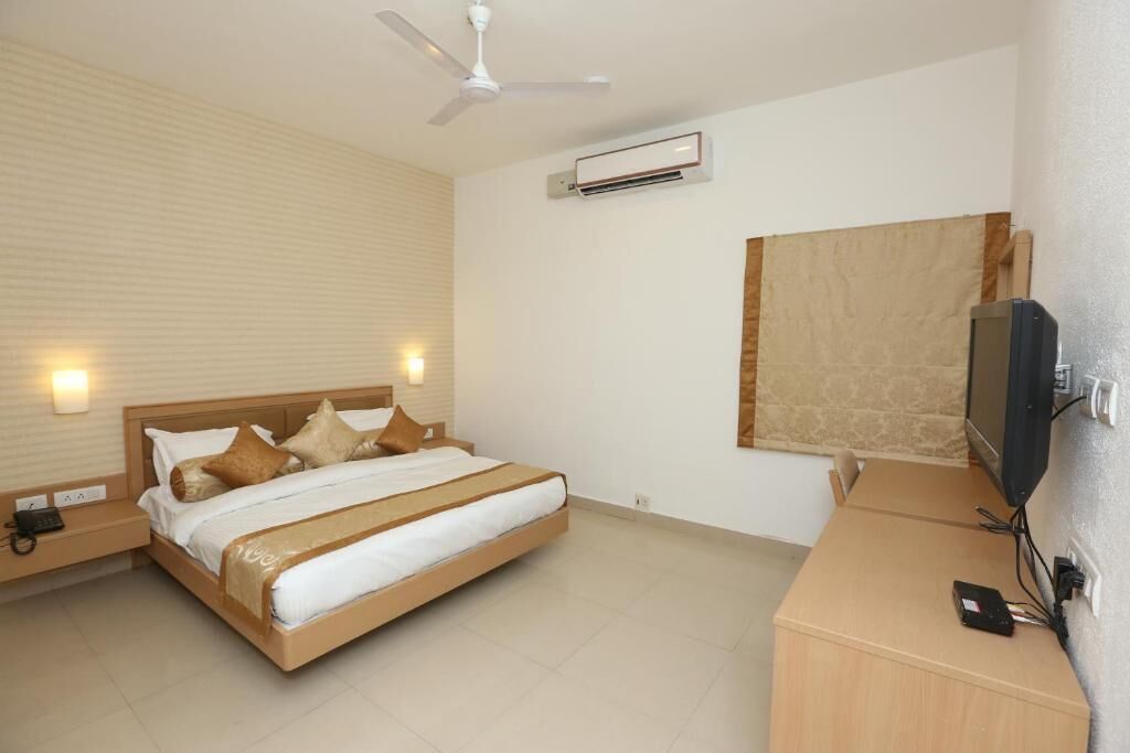 Una habitación de hotel con una cama, mesitas de noche, un televisor, un equipo de aire acondicionado y un ventilador de techo.