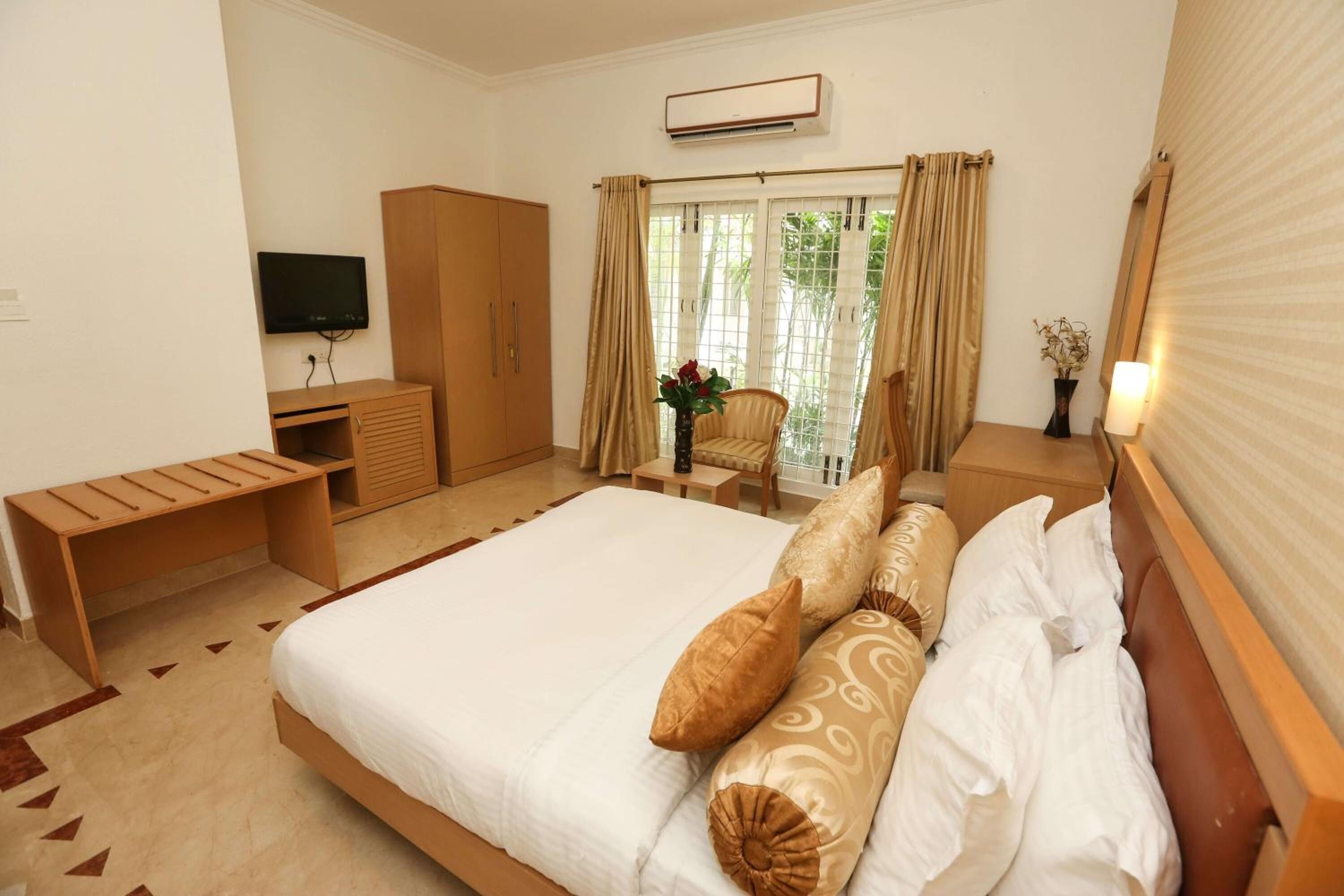 Une chambre d’hôtel avec un grand lit, un bureau en bois, une télévision, une armoire et une fenêtre avec des rideaux.