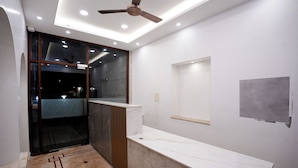 A modern bathroom with a marble countertop, a ceiling fan, recessed lighting, and a glass shower enclosure. - Avenue 11 Boutique Residences (Chennai)