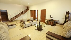 A spacious living room with a sofa set, a glass coffee table, a wooden side table, and a staircase leading to another level. - Avenue 11 Boutique Residences (Chennai)