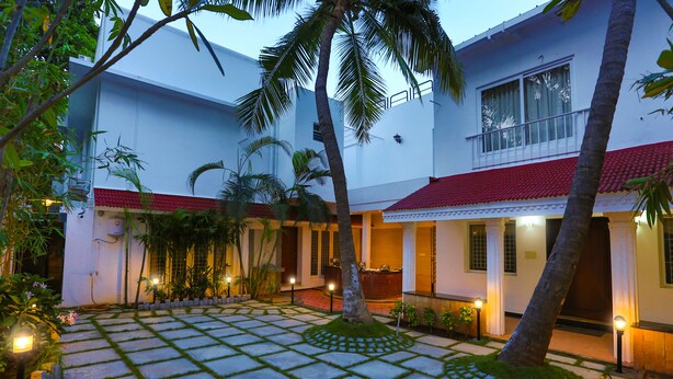 A courtyard with a tiled floor, palm trees, and a building with a red roof. - Avenue 11 Boutique Residences (Chennai)