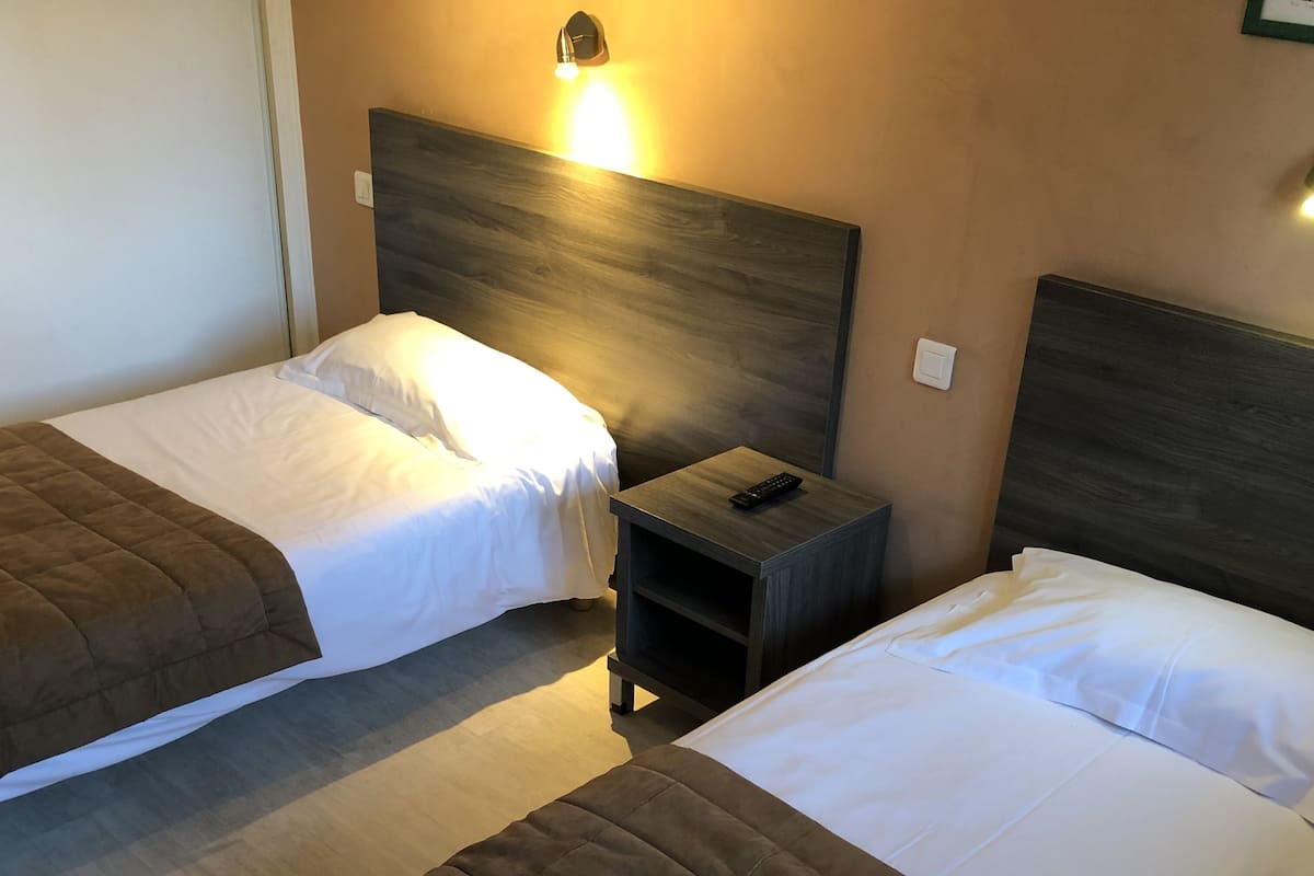 Deux lits simples avec des têtes de lit marron, du linge de lit blanc et une table de chevet avec une télécommande.