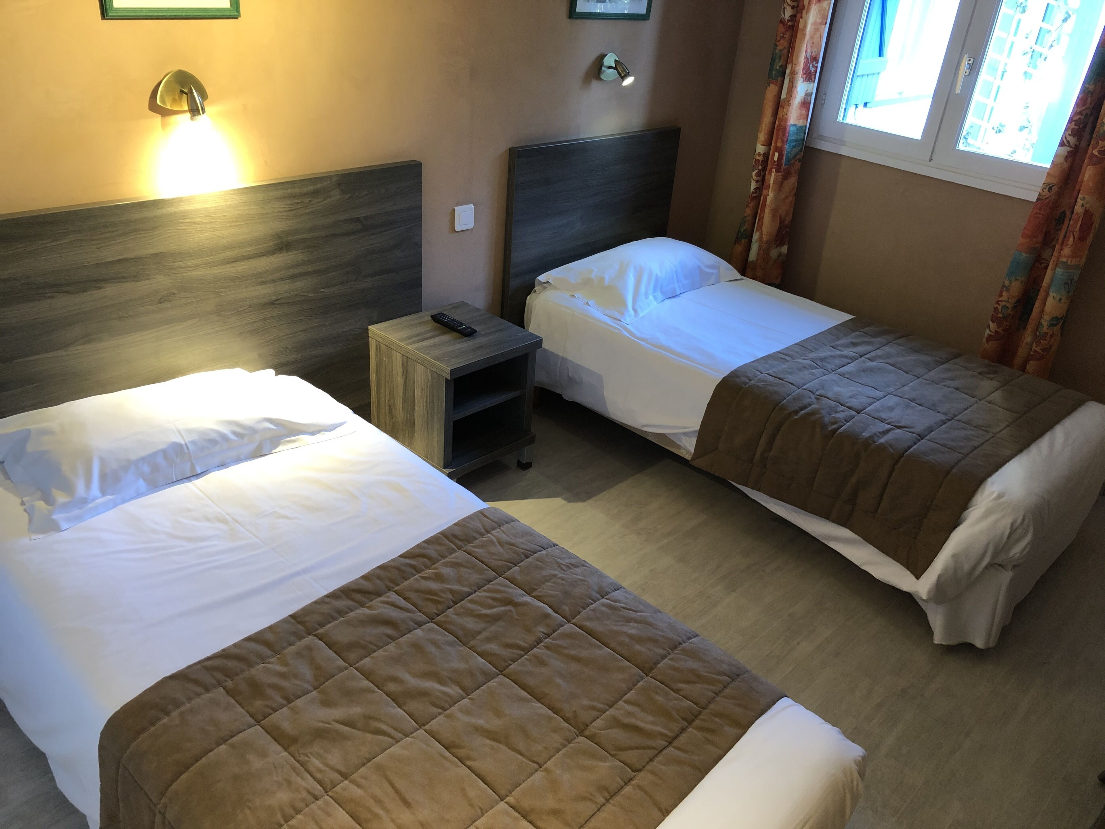 Habitación de hotel con dos camas, una mesita de noche, una lámpara de pared y una ventana con cortinas.
