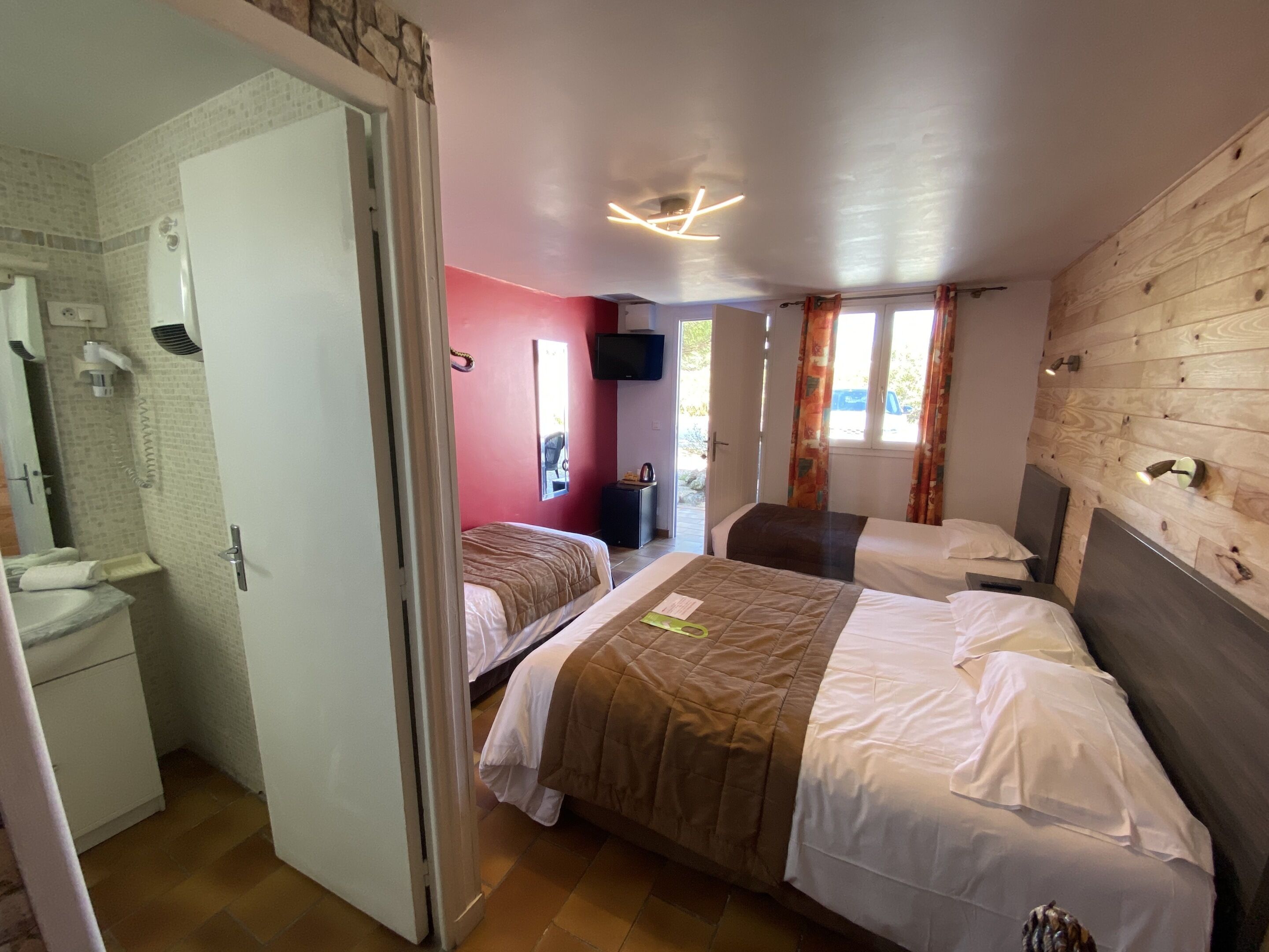 Habitación de hotel con dos camas, baño, televisor y pared de madera.