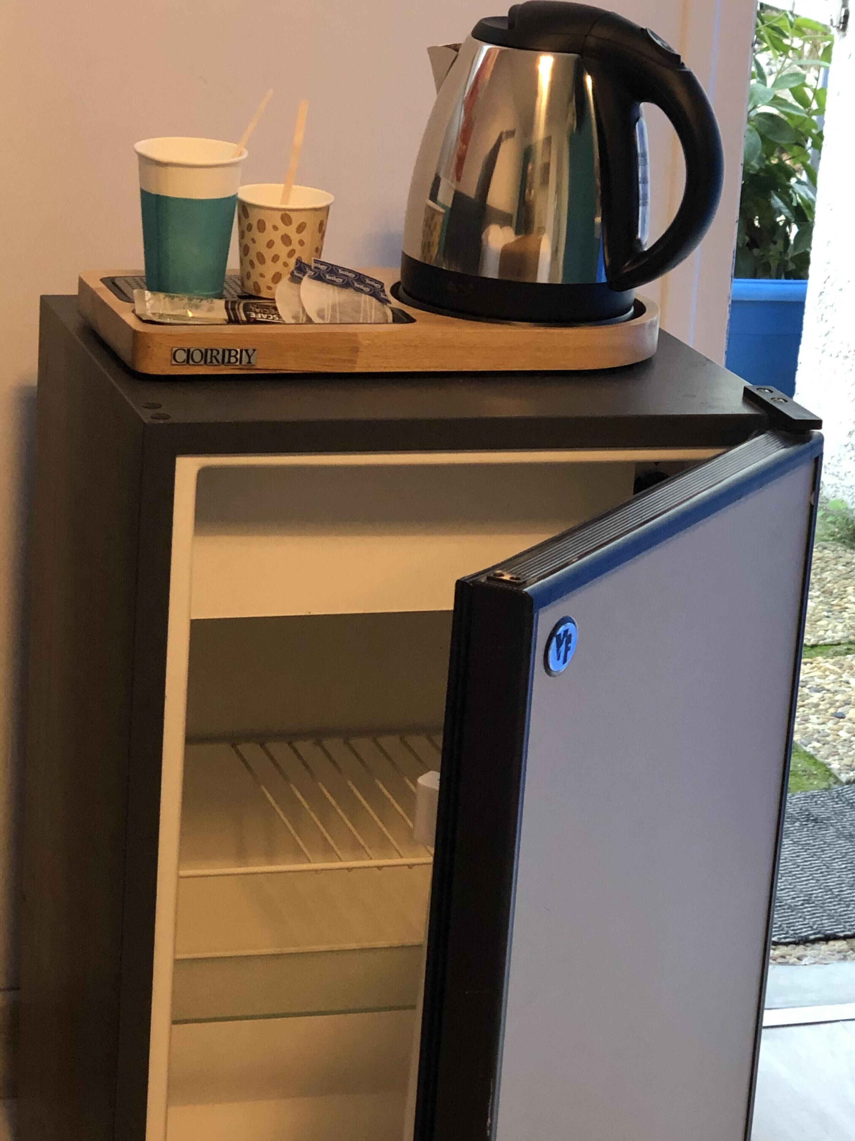 Een kleine koelkast met een koffiezetapparaat en wegwerpbekers erboven.