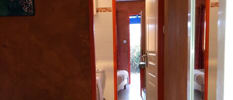 Habitación de hotel con cama, una mesita y vistas al baño y al pasillo.