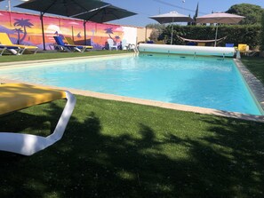 A swimming pool with lounge chairs and umbrellas, surrounded by a grassy area and a mural.