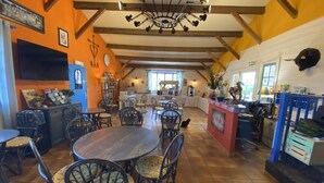 Un restaurant chaleureux avec des tables et des chaises en bois, une salle à manger centrale et une cuisine visible à travers le mur du fond.
