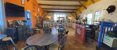 Un restaurante acogedor con mesas y sillas de madera, un área de comedor central y una cocina visible a través de la pared de fondo.