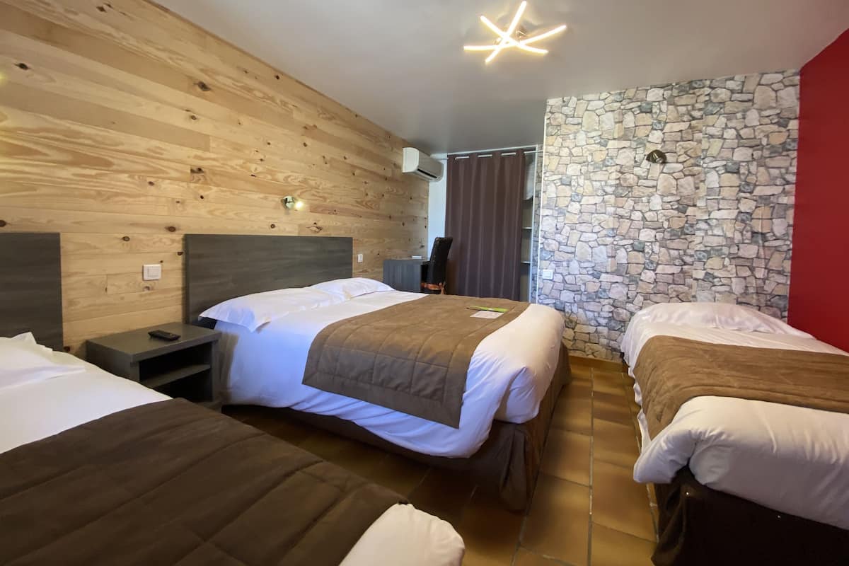 Une chambre d’hôtel avec trois lits, des murs lambrissés en bois, un mur en pierre et un luminaire moderne au plafond.