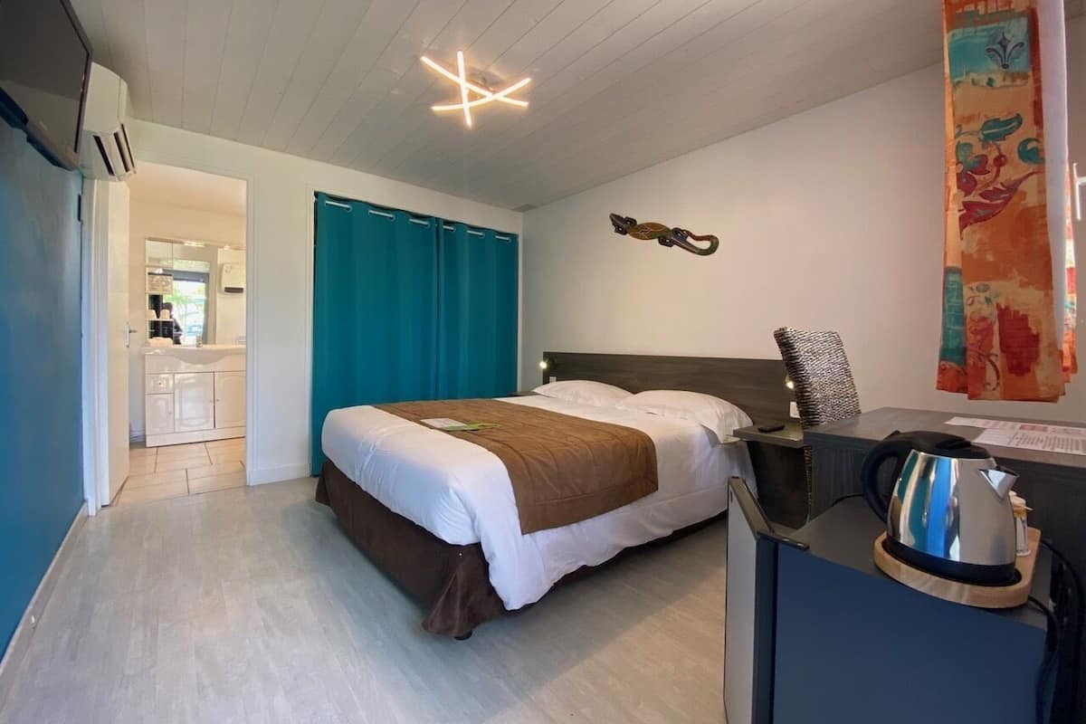 Une chambre d’hôtel avec un lit, un bureau doté d’une bouilloire, et une salle de bain visible au fond.