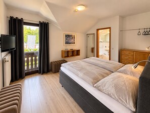 A bedroom with a bed, a TV, a wooden cabinet, and a view of the outdoors. - Landhotel Linden am Venekotensee (Niederkruechten)