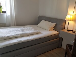A neatly made bed with white linens, a grey headboard, and a bedside table with a lamp. - Landhotel Linden am Venekotensee (Niederkruechten)