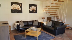 Un salón con dos sofás de cuero negro, una mesa de centro de madera y una escalera con barandillas blancas.