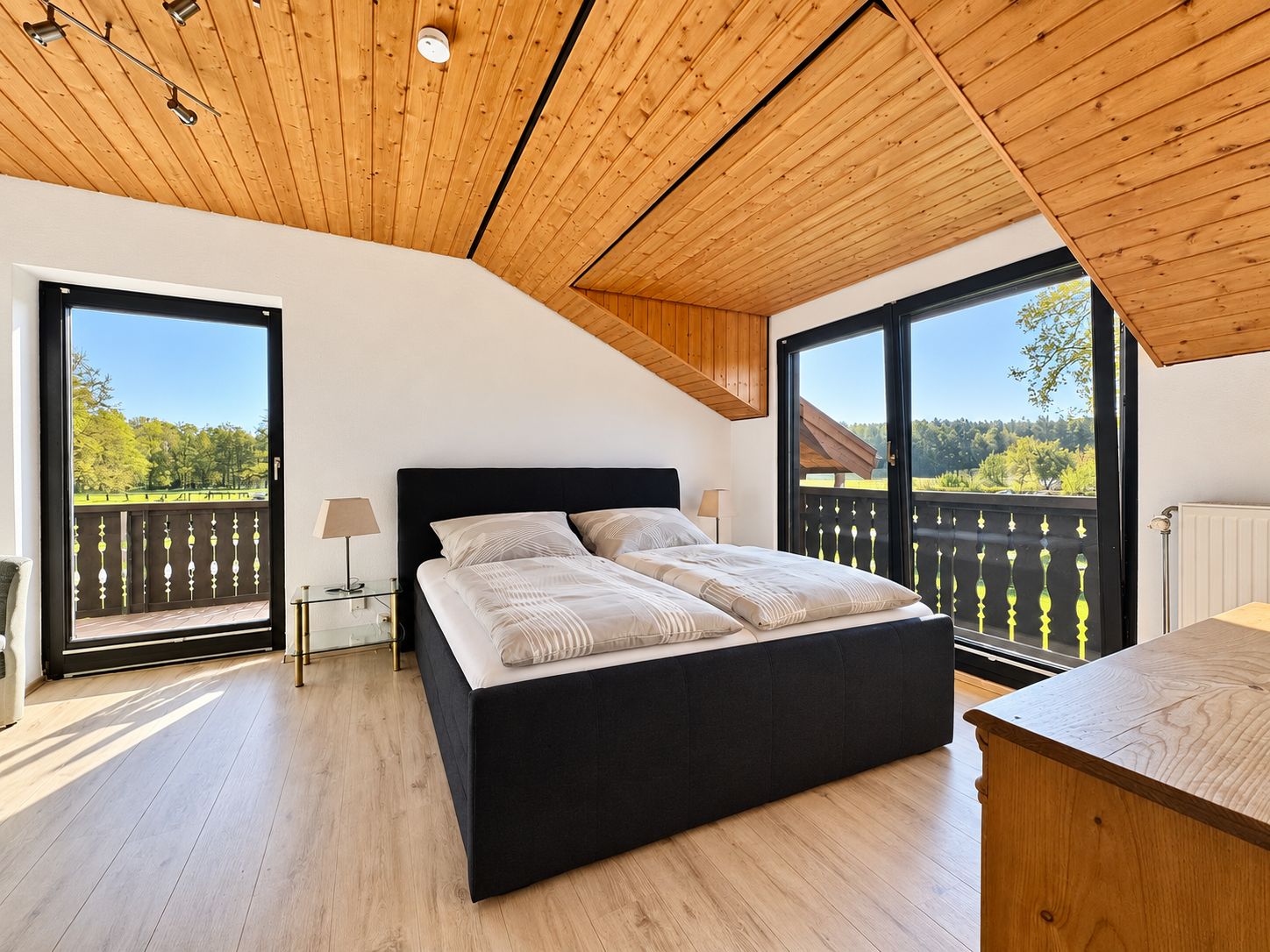 Ein Schlafzimmer mit einem großen Bett, einer Holzbalkendecke und Blick auf einen Park durch eine Schiebetür.