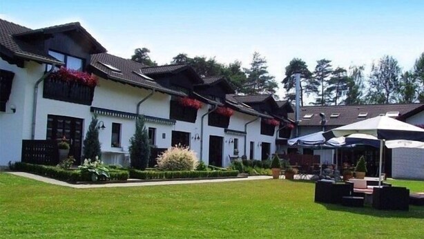 Una hilera de edificios blancos con techos oscuros, un césped y zonas de estar al aire libre.