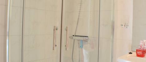 A glass-enclosed shower with a white sink and toiletries.