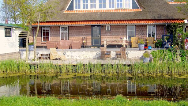 A traditional house with a thatched roof, a brick facade, and a pond in the foreground. - Appartementenboerderij Nieuwesluis (Wieringerwaard)