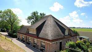 A traditional brick building with a steeply pitched thatched roof, large windows, and a paved driveway. - Appartementenboerderij Nieuwesluis (Wieringerwaard)