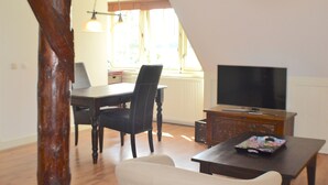 A dining area with a table and chairs, a TV on a stand, and a window with natural light. - Appartementenboerderij Nieuwesluis (Wieringerwaard)